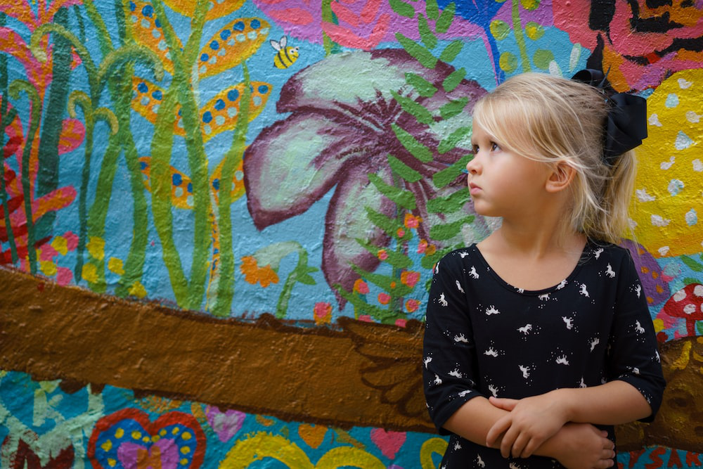 A colourful wall mural with a young girl standing in front of it.