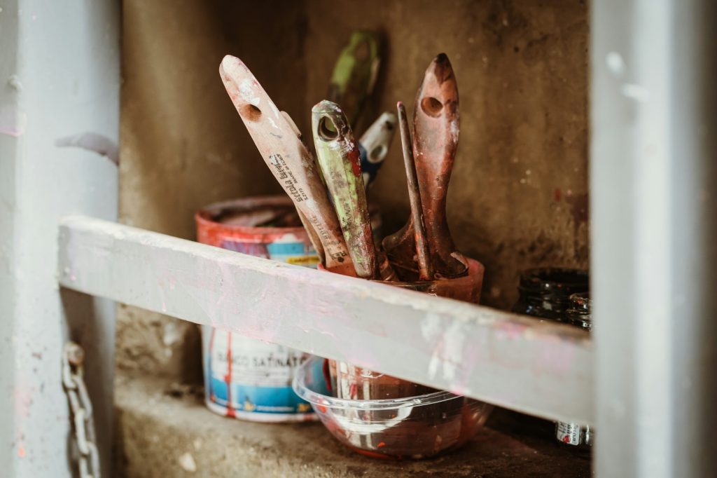 A variety of paint brushes in a bucket