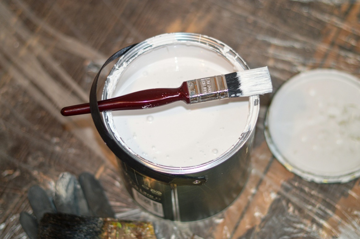 A paintbrush resting on a white paint bucket