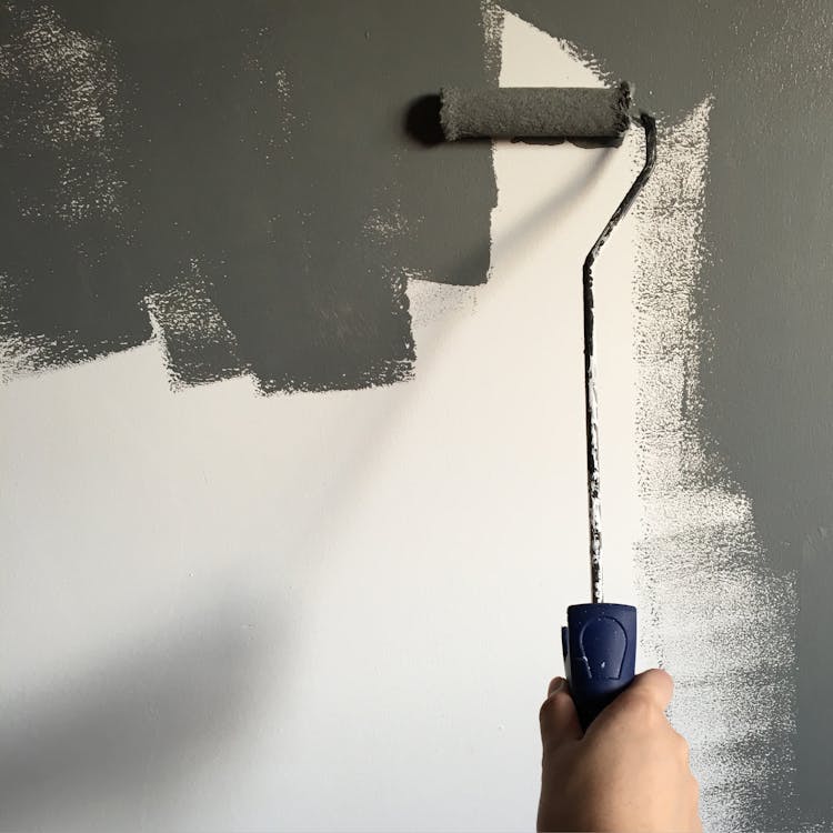 Person holding a paint roller while applying eco-friendly, low-VOC paint on a wall