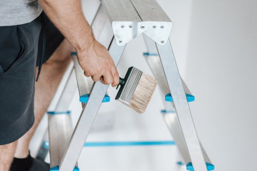 Person standing on a ladder holding a paintbrush