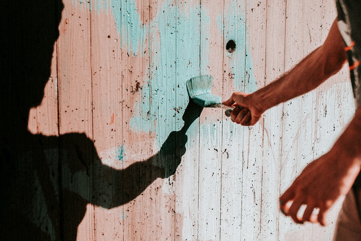 A person painting a wooden fence