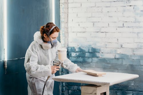 Woman painting a piece of wood wearing safety gear, highlighting safe practices