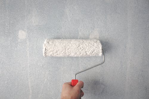 A person holding a paint roller, preparing to paint the exterior of a building.