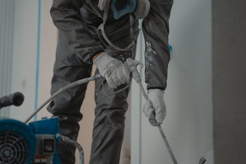 A person using a power sprayer to paint the exterior of a building.