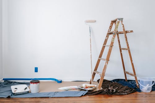 Ladder with painting supplies set up for residential painting, including brushes, rollers, and paint cans.