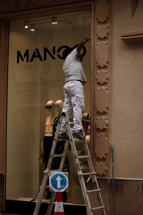 A painter working on the exterior wall of a shop.