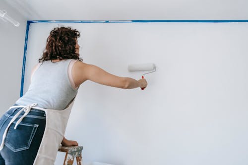 Person painting an interior wall with a roller, focusing on creating an even, high-quality finish.