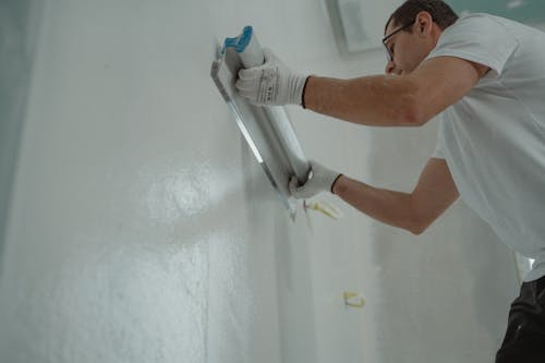 Person painting an interior wall, creating a sense of spaciousness with light-colored paint.