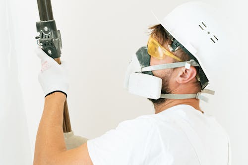 A person wearing a mask while painting an interior wall, taking safety measures for indoor painting.