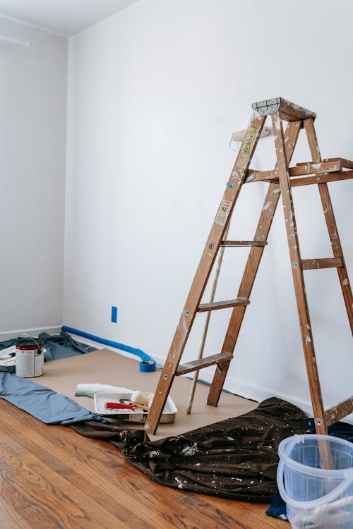 Various painting tools, including brushes, rollers, and a ladder, arranged for a residential painting project.