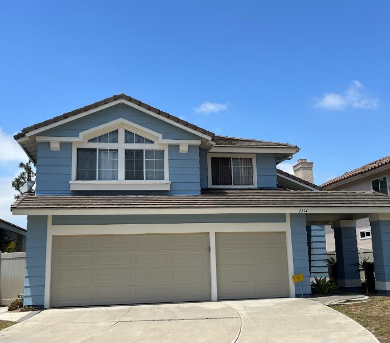 A light blue two-story house with beige garage doors and a brown-tiled roof.