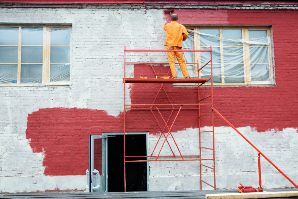 Professional painter applying exterior paint to highlight architectural features of a commercial building.